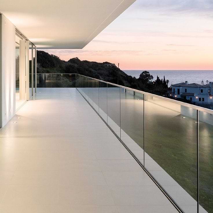 Sleek glass deck railing on a luxury balcony overlooking the ocean at sunset, offering unobstructed views and modern aesthetics.